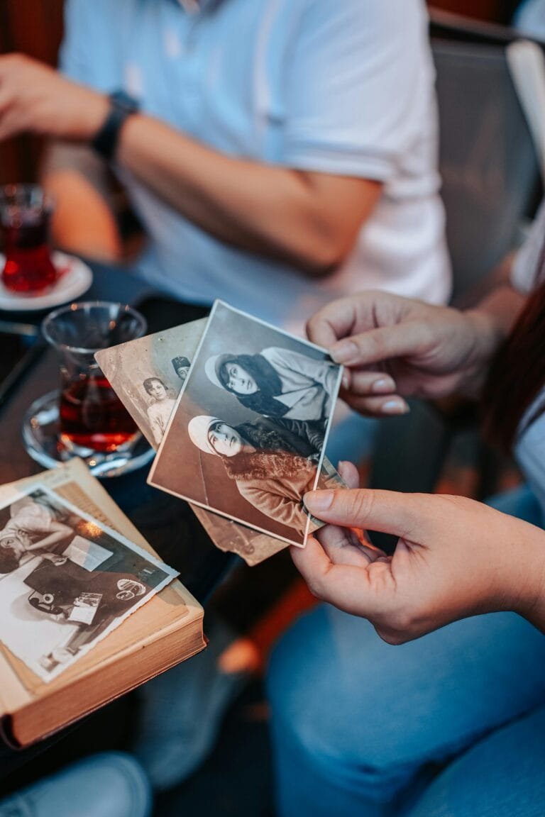 Duas pessoas observando fotografias antigas de familia em preto e branco durante pesquisa genealogica
